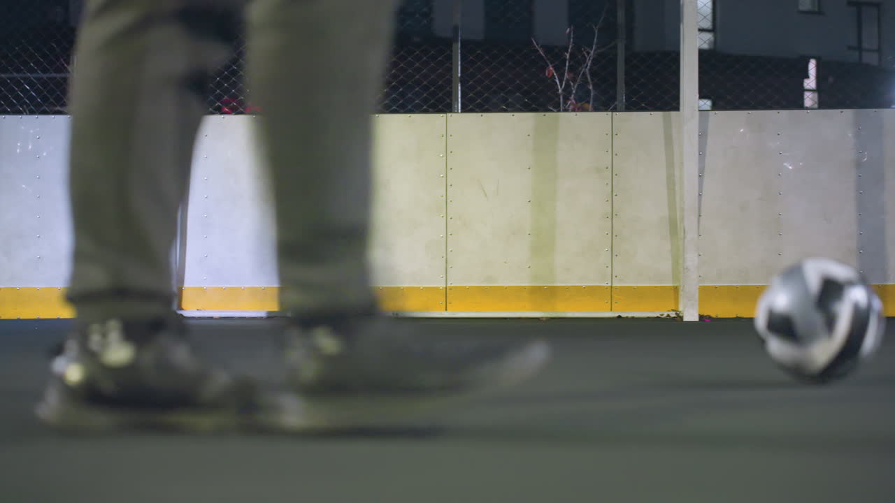 스포츠 경기장에서 굴러가는 축구공은 운동화를 입은 선수에 의해 혀 있으며, 골포스트와 빛나는 벽이 배경으로 게임의 통제, 운동 및 에너지를 보여줍니다.