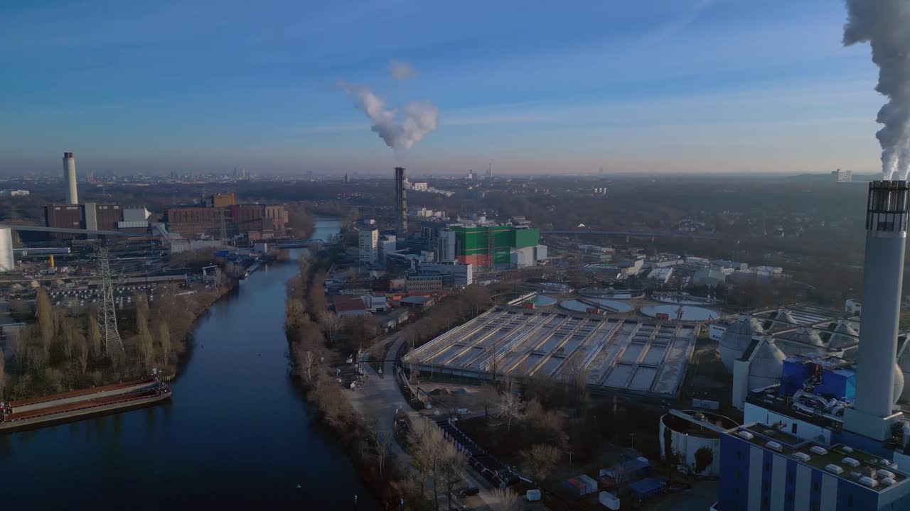 Kaupunkijätteen energiajalostuslaitos, jossa suuret savupiiput päästävät höyryä kirkkaan siniselle taivaalle, mikä havainnollistaa kestävää kaupunkikehitystä. Kaunis ilmakuva, jossa panoraama pyörii vasemmalle dronen avulla.