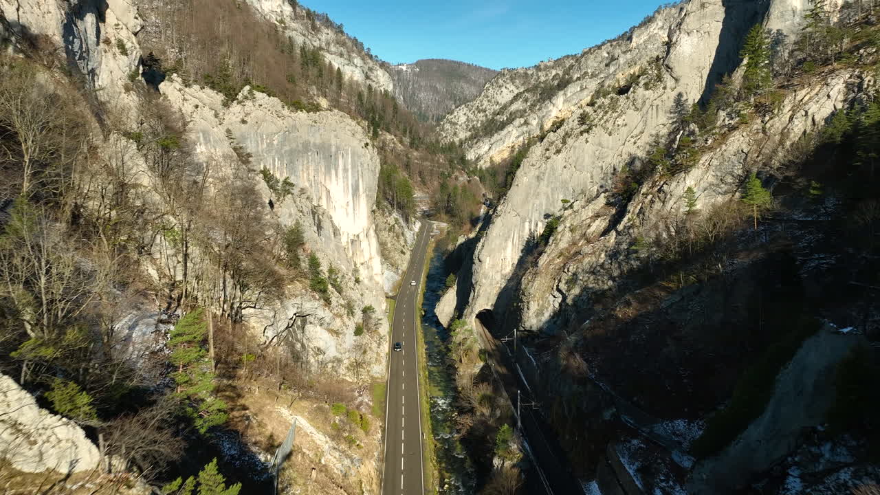 Auto che percorrono la strada nelle Gole del Giura a Moutier, in Svizzera, in una fredda e soleggiata giornata autunnale con neve nelle zone d'ombra.