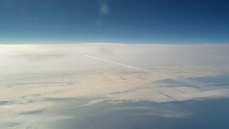 Incredible-view-from-the-cockpit-of-an-airplane-flying-high-above-the-clouds-leaving-a-long-white-condensation-vapour-air-trail-in-the-blue-sky