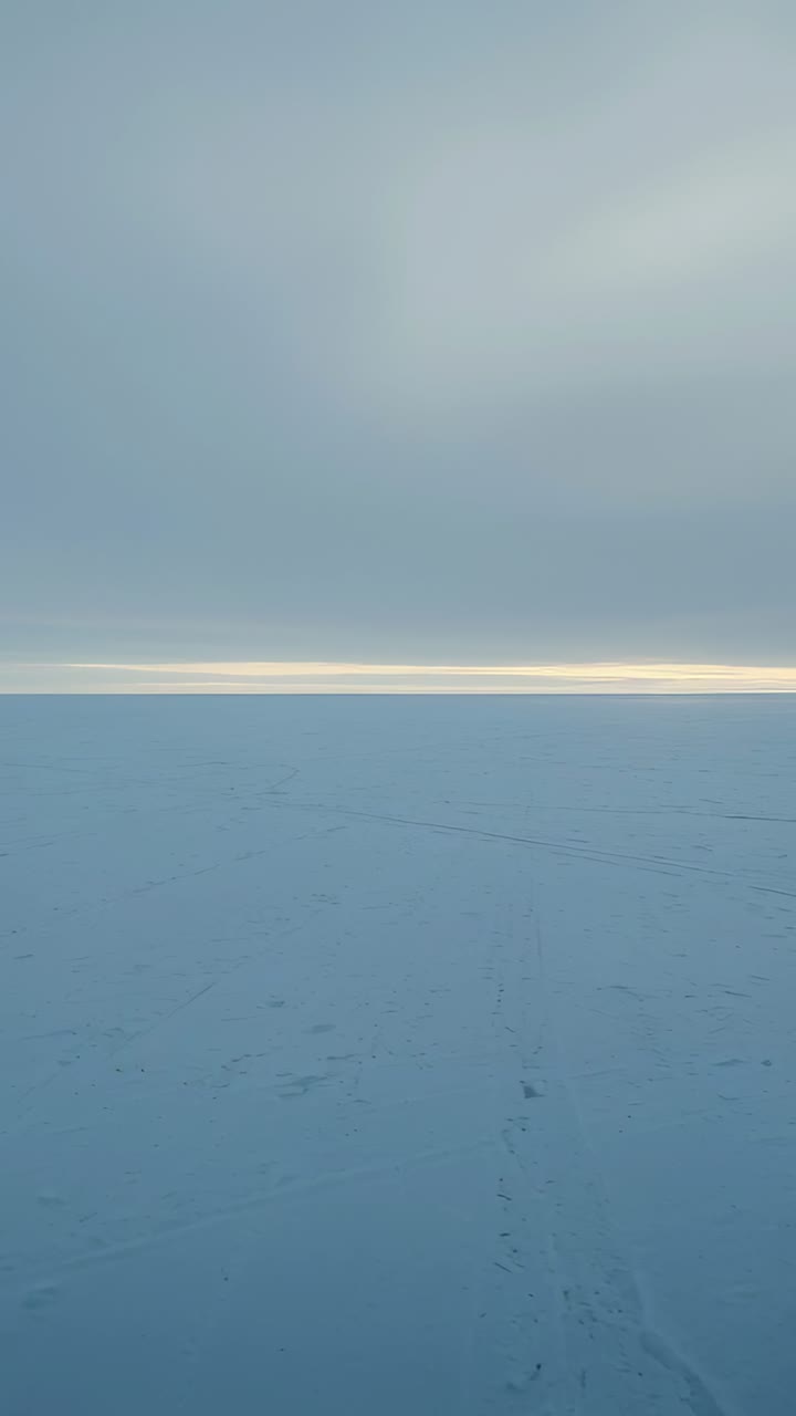 Vertical video: Drone filming at icy plain showing thin horizon band shifting and tracks for study