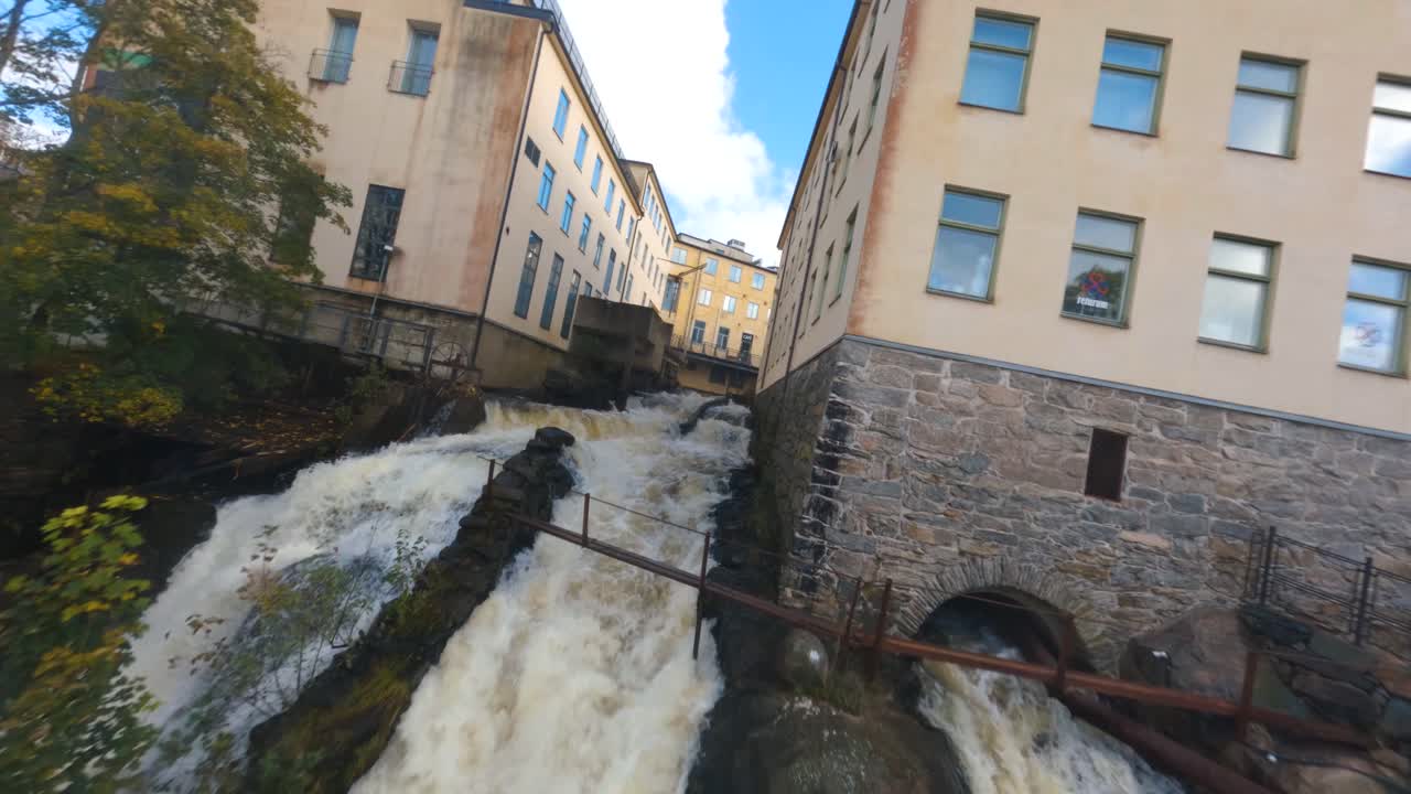 FPV drone proximity flight over a waterfall between old industrial buildings
