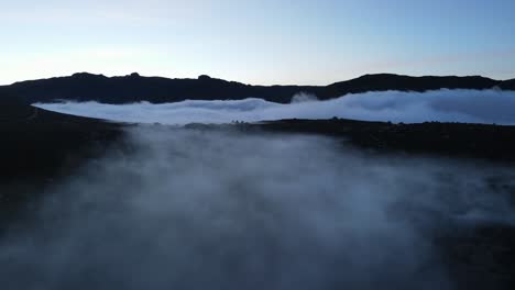 vista aérea de un valle de montaña rocoso cubierto de niebla y nubes