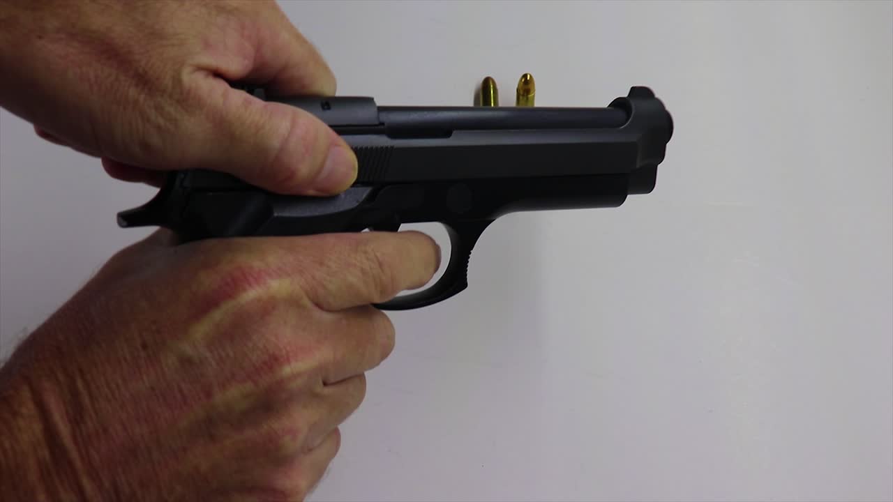 recogiendo un arma de fuego negra y armándola dejando una mesa de balas