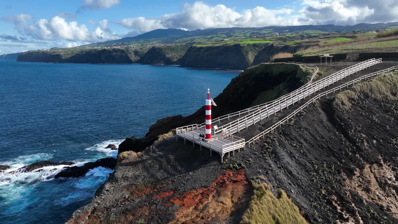 Small lighthouse on rugged cliff line of the Azores, Sao Miguel, shipping beacon, vulcanic rocks, aerial drone video