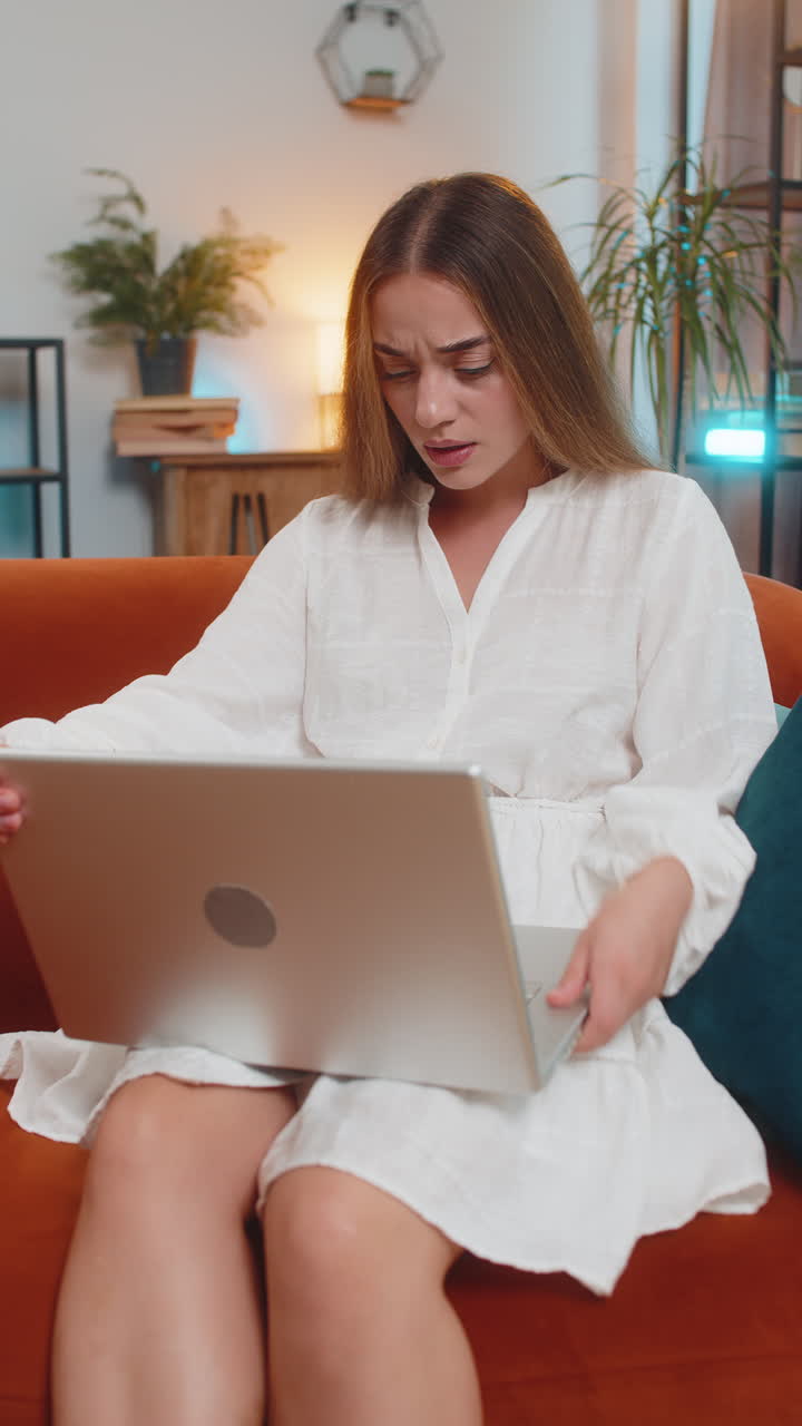 Angry young woman using laptop feel frustrated mad about computer problem sitting on sofa at home