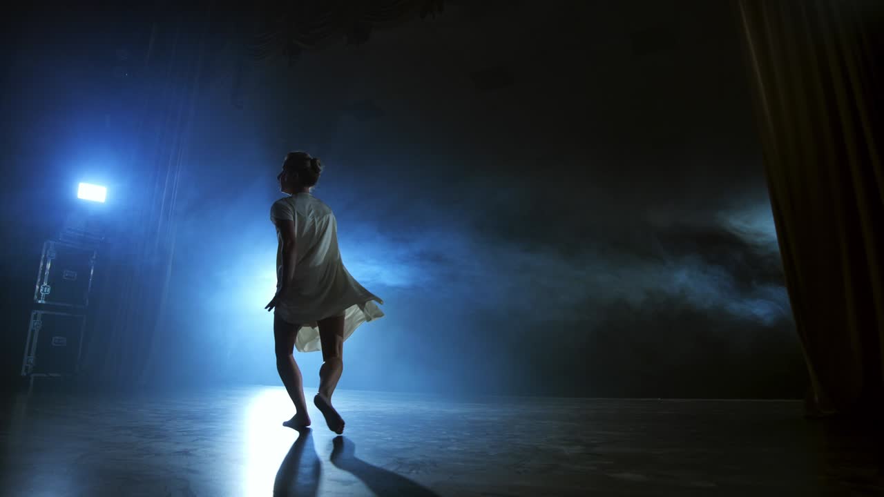 Modern ballet dancing woman barefoot doing spins and pirouettes and dance steps standing on stage in smoke in slow motion. Performance on stage