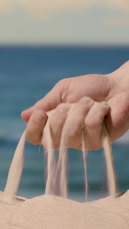 video concepto vertical de vacaciones de verano con la mano recogiendo arena de la playa contra el fondo del mar