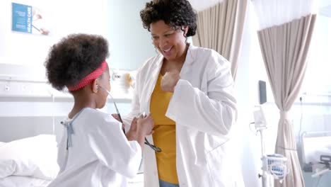 happy african american female doctor fooling with girl in hospital room, slow motion