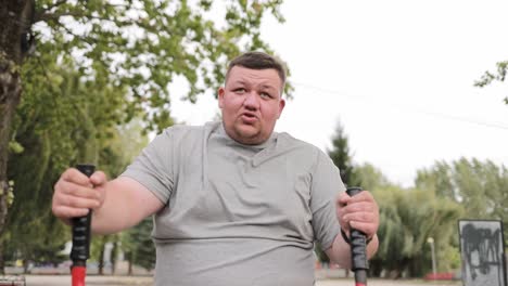 persistent overweight man in gray tshirt running on exercise machine outdoors in green area persistent satisfied overweight man in gray tshirt running on exercise machine outdoors in green area a fat man loses weight by exercising on an outdoor exercise machine