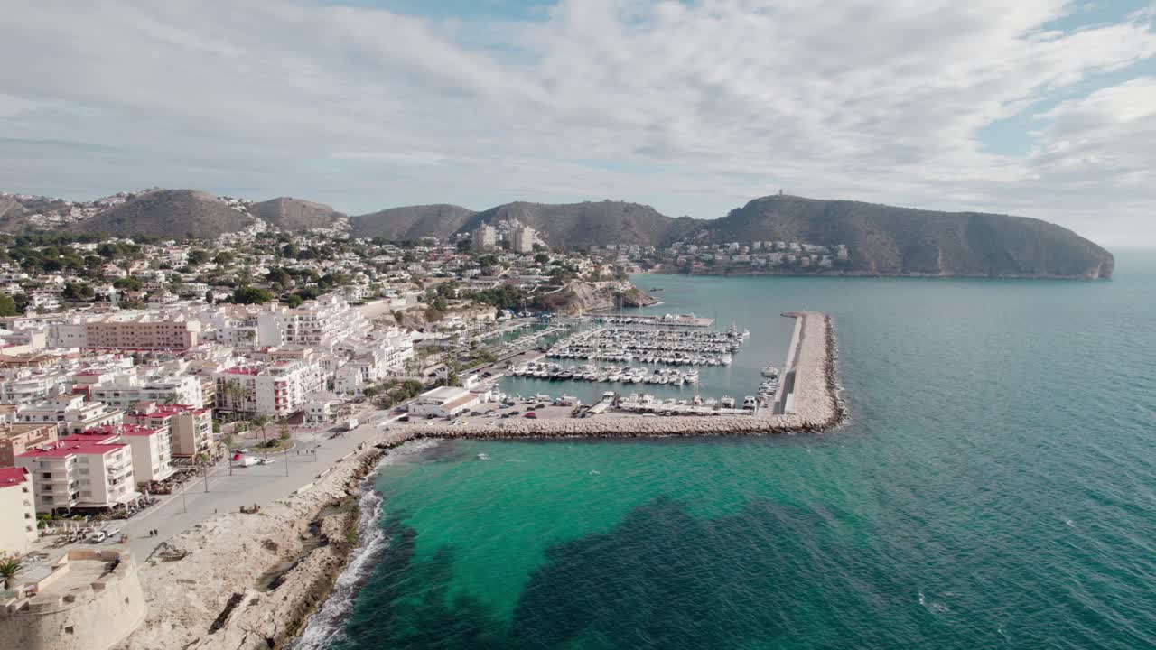 Marina With Boats And Breakwater In Coastal Town Of Moraira In Spain. Rolling Hills In Background. wide aerial shot