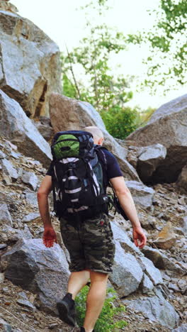 a traveler with a backpack on his shoulders rises to the top of the mountain with stones in the afternoon in warm weather. tourism. vertical video