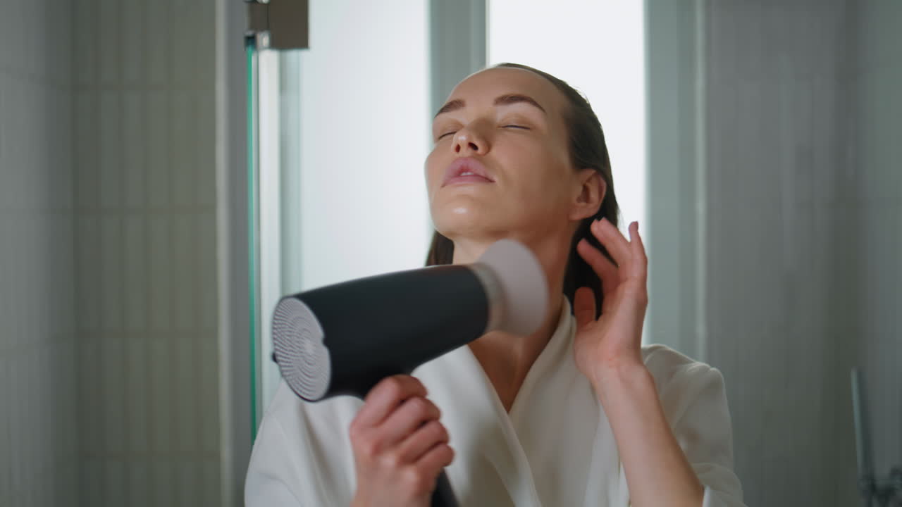 Lady blowing wet hair looking camera closeup. Smiling woman preparing in morning