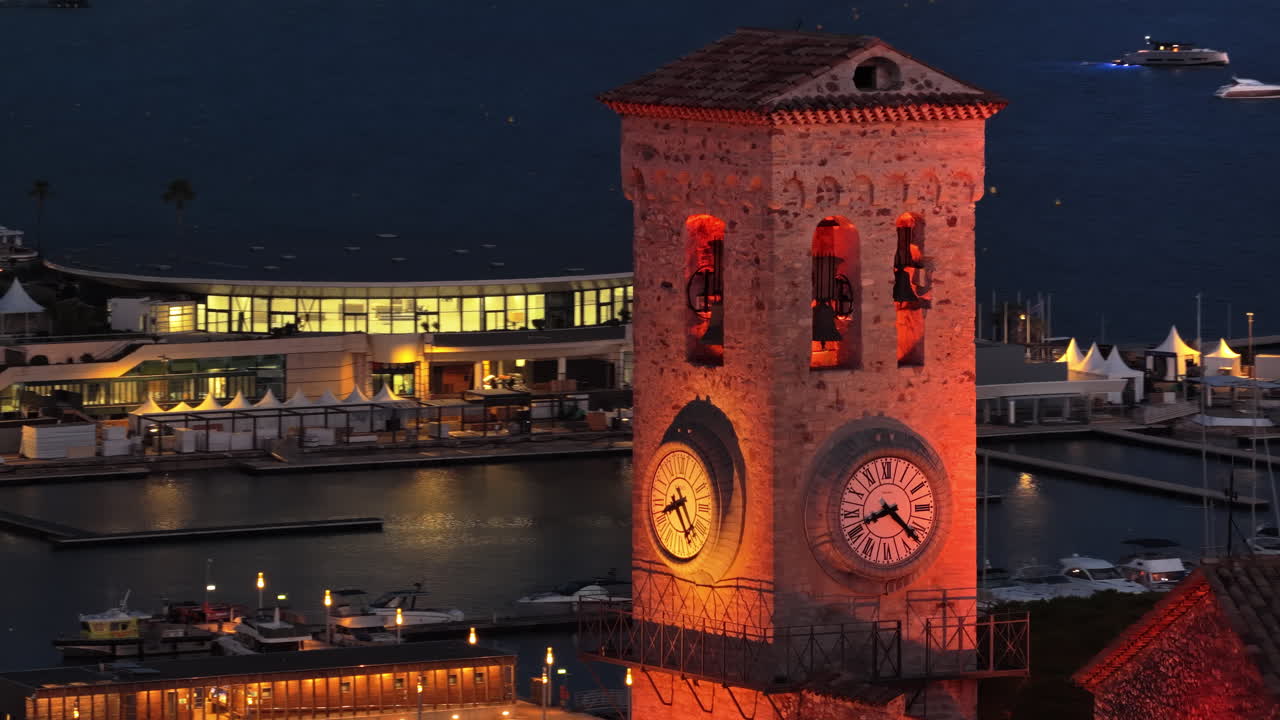 Aerial drone view of the historic Cannes clock tower at dusk, with the bustling city center in the background, glowing with evening lights