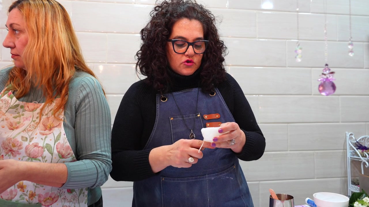 Twee vrouwen met schorten aan leren de kunst van het maken van geurkaarsen tijdens een creatieve workshop.