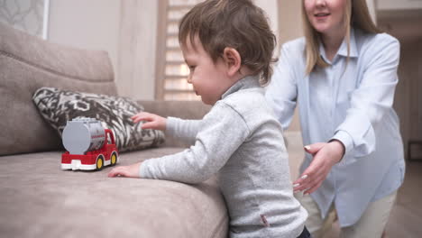 baby taking his first steps near the sofa to take a fire truck toy