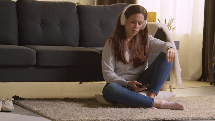 Woman Wearing Wireless Headphones Sitting On Floor At Home Streaming Music From Mobile Phone 8
