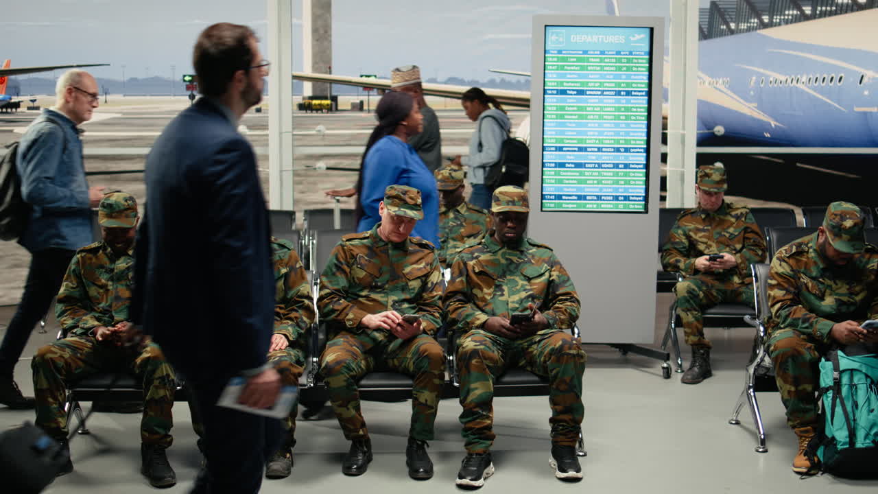 Militari diversi seduti su una panca nella sala d'attesa dell'aeroporto che discutono.