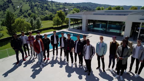 group of men posing in front of a luxury home and pool