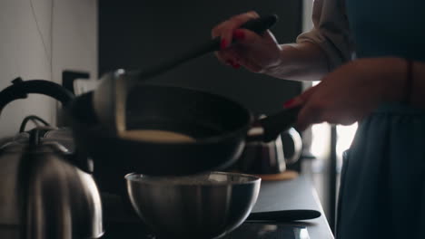 Frau-Brät-Pfannkuchen-Zum-Frühstück.-Hausfrau-Gießt-Teig-In-Eine-Bratpfanne,-Die-Neben-Dem-Herd-Steht