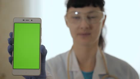 close up de pantalla verde en el teléfono sostenido por el científico. mujer médico sosteniendo el teléfono con pantalla verde hasta la cámara para la composición. mujer profesional médico mostrando teléfono inteligente móvil con pantalla verde.