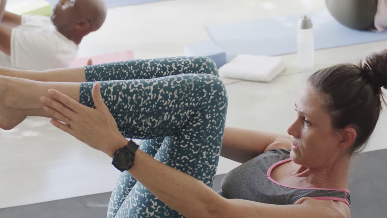 concentrados en ancianos diversos haciendo pilates, estirándose en esteras con una entrenadora, sin alteración, en cámara lenta