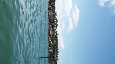 A-small-canoe-rowing-past-screen,-sailing-towards-the-tropical-coastal-town-of-Barra-do-Cunhaú-in-Rio-Grande-do-Norte,-Brazil-from-the-tropical-Restinga-beach-on-a-sunny-summer-day