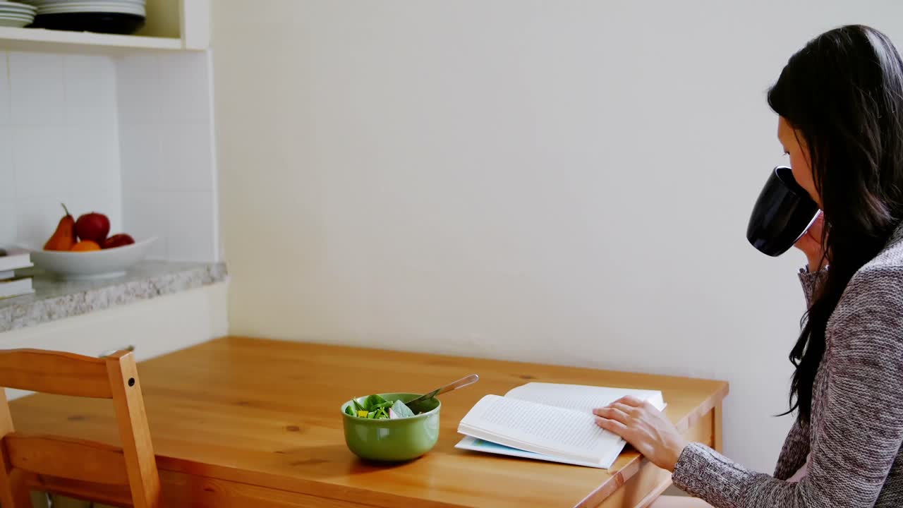 mujer leyendo un libro mientras toma café en la cocina