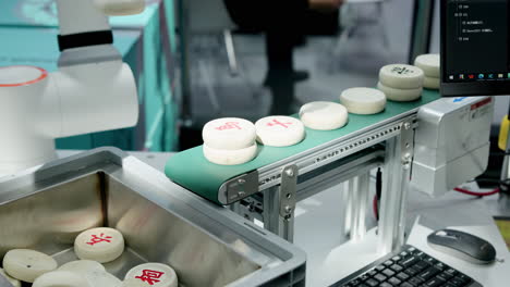 robotic arm handling chinese chess pieces on an automated conveyor belt