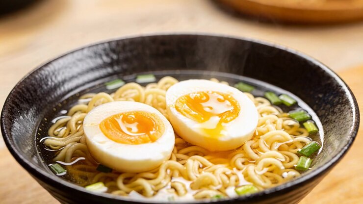Mani dello chef che affettano uova con un coltello da chef sul bancone, impiattando ramen con tuorli liquidi.