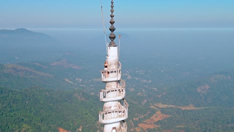 vertical shot of a woman standing at the top of the iconic ambuluwawa tower in kandy, sri lanka. surrounded by panoramic views of mountains and misty skies.