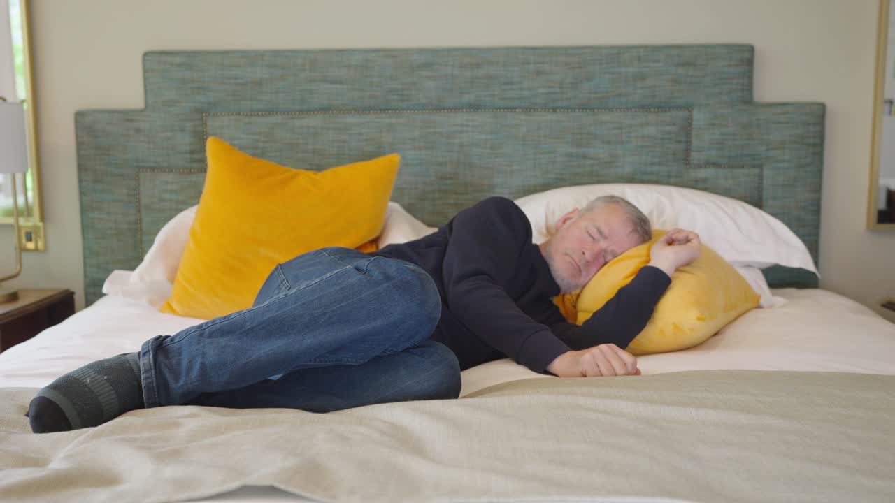 Man wearing clothes lying across double bed trying to sleep, locked off