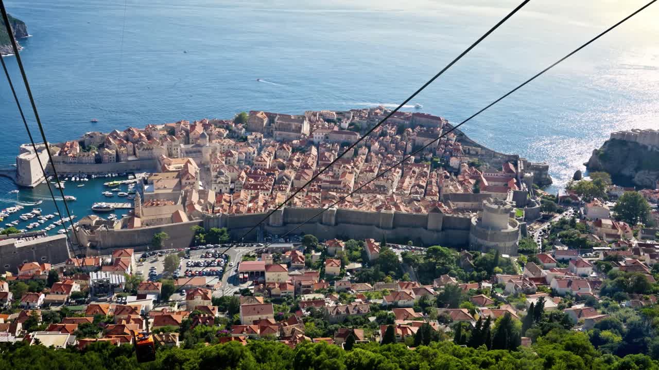 Landscape view from a descending cable car over Dubrovnik’s Old Town, showing terracotta rooftops, winding streets, and the sparkling blue Adriatic Sea under bright sunlight