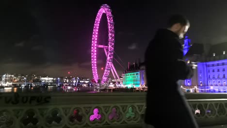 time lapse of the london eye from the westminster bridge at night whilst tourists and locals walk through the shot