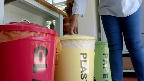 una mujer biracial sénior segregando la basura en casa, en cámara lenta.