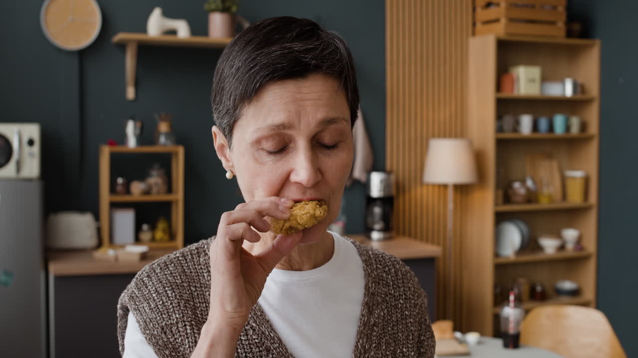 Senior woman enjoying a snack and drink in her kitchen
