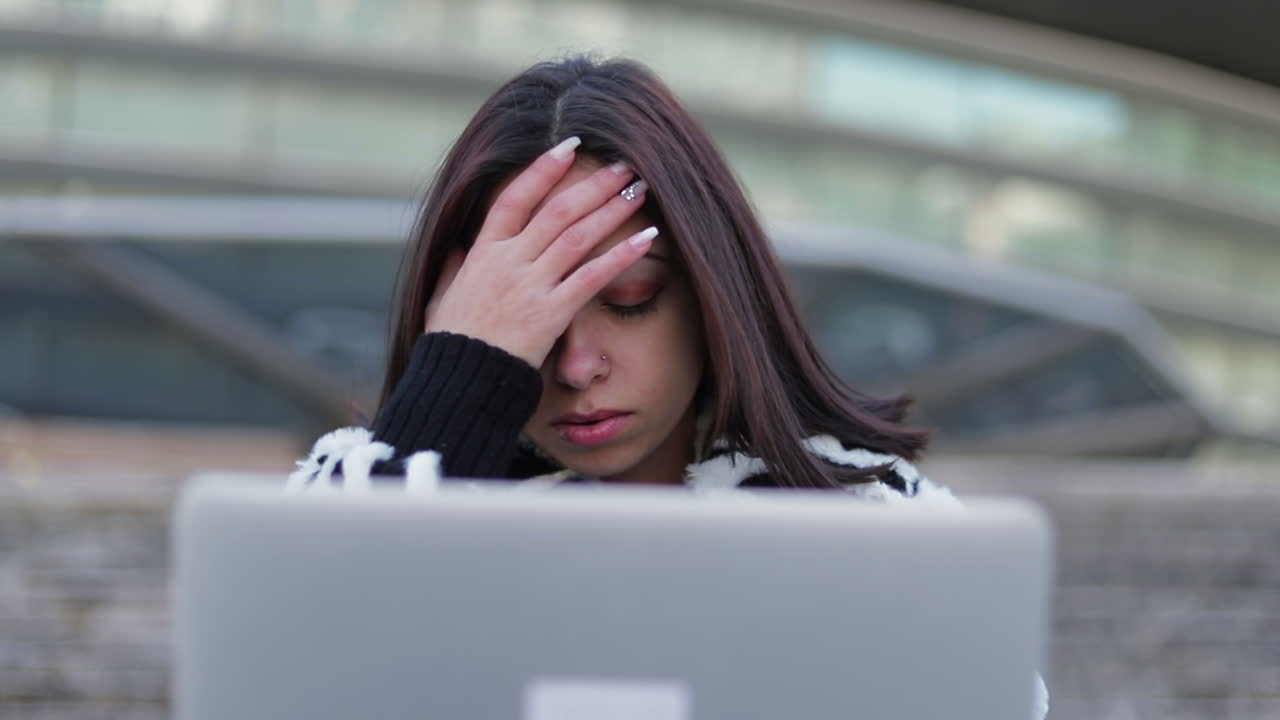 hermosa morena cansada mirando la computadora portátil y frotando la cara