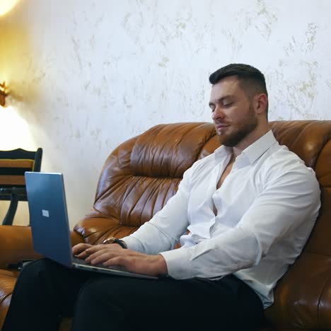 handsome young businessman works on laptop in a hotel room. man isresting after businessmeeting and surfing internet