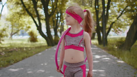 active athletic fitness toddler girl walking with hula hoop circle ring on hand in city morning park