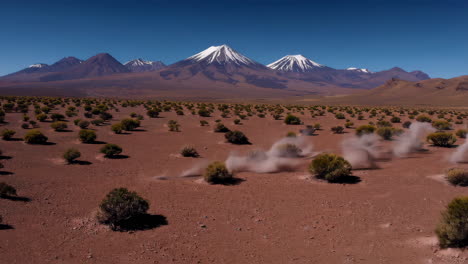 vast arid landscape with snow-capped mountains and dust plumes