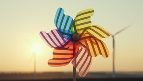 pinwheel rotate color plastic, windmill with blowing wind against  of wind turbines wind park sunset sky of sunny day summer. descending bright disk of sun beyond horizon on field. lens flare. relax