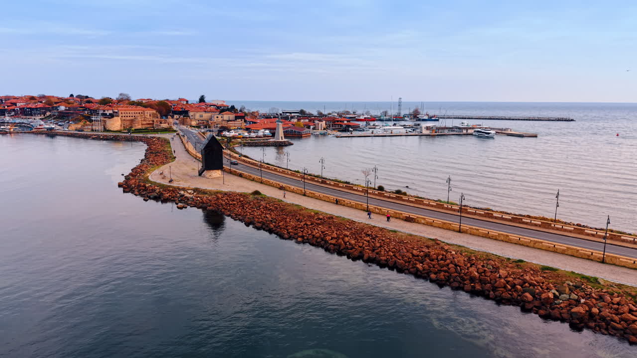 Pessoas caminham pela estrada de chão ao longo da rodovia na barragem através da paisagem marítima. Paisagem urbana de Nessebar, Bulgária, vista de drone
