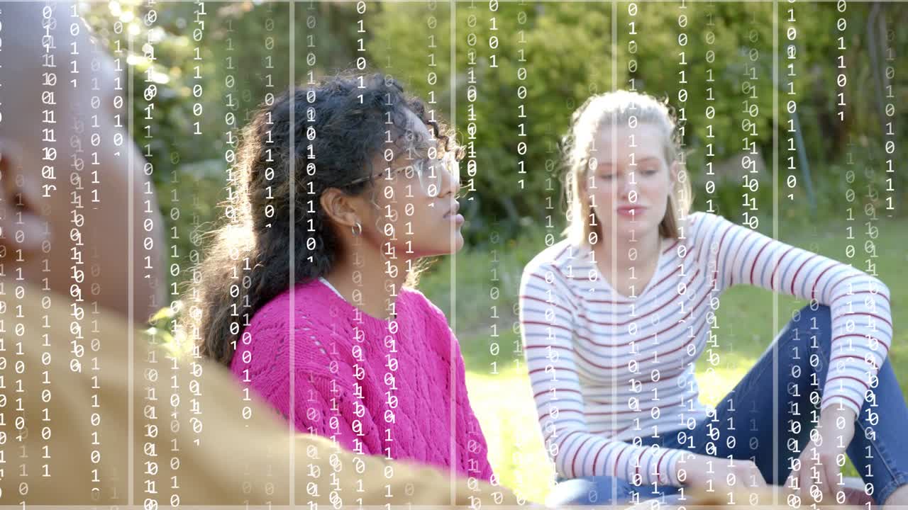 Teenage duo socializing in park as blurred friend gesturing, binary digits rising, showing tech
