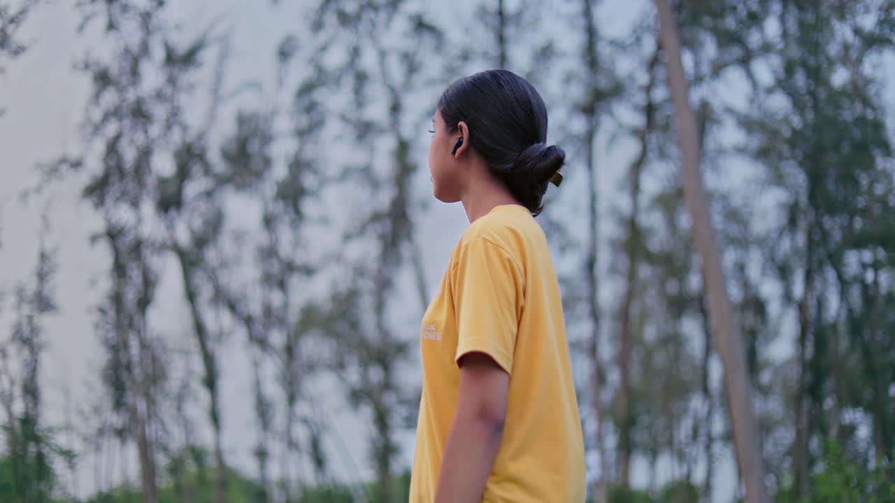 Female adventurer standing alone in a forest wearing earpods and looking at the scenic view, exploring nature and enjoying peaceful landscape view