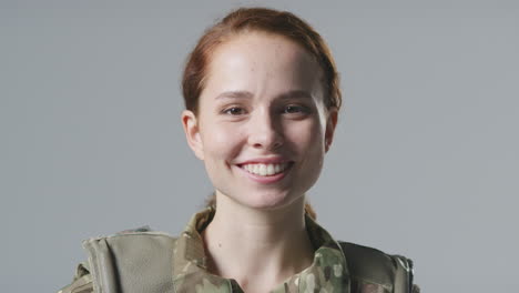 studio portrait of smiling young female soldier in military uniform against plain background