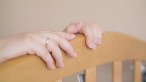 careful-mother-hands-rock-wooden-crib-in-light-room-closeup