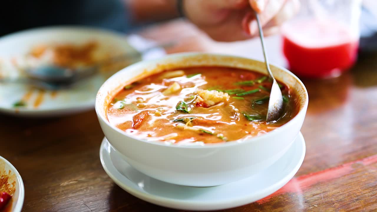 una persona saborea la sopa tom yum en un entorno vibrante, destacando los ricos colores y texturas del plato bajo luz natural