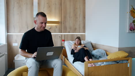 married couple in the maternity hospital ward. woman takes care of a baby and her husband works on laptop.