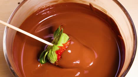 strawberry being dipped into melted chocolate