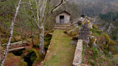 Cabaña-De-Montaña-Con-Muro-De-Piedra-En-El-Acantilado-Del-Mirador-Con-Puente-Y-Mesas-De-Madera-En-La-Zona-De-Picnic-Con-Bosque-De-Robles